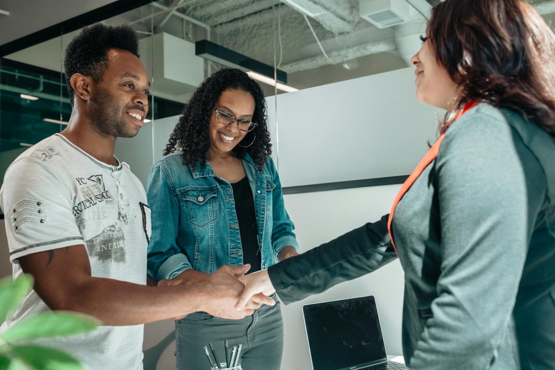 Smiling couple shaking hands with a professional in a modern office setting.
