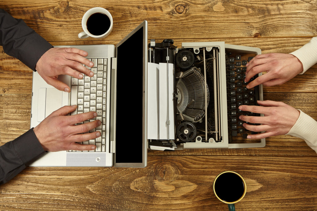 Old vs New Tech Typing – Side-by-side hands type on a laptop and a typewriter, contrasting modern and vintage tools.