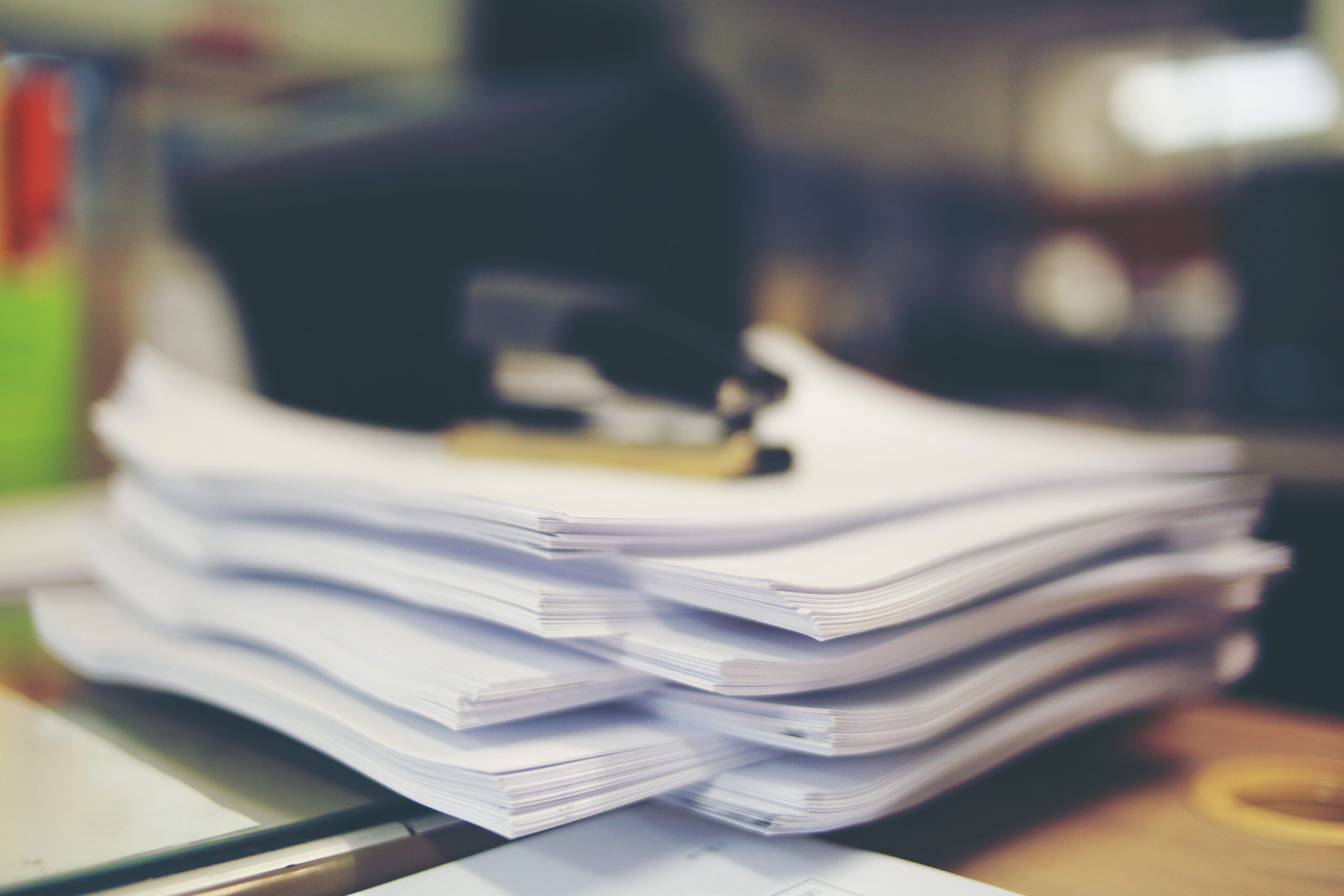 Stack of printed documents on an office desk with a stapler on top.